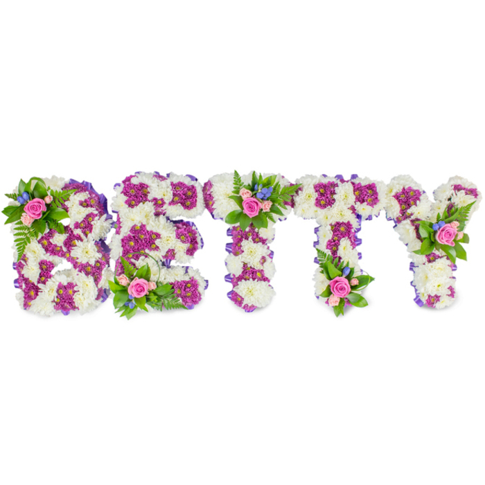 A bespoke memorial piece carefully composed to read BETTY in large, freestanding capital letters, crafted by an experienced florist for sympathy and remembrance. The principal surface of each letter is a dense field of creamy-white chrysanthemums, selected for their full, snowball-like heads that create a plush, cloud-soft texture and reflect a cool, even studio light. To define each character with distinction, clusters of vibrant fuchsia to deep purple chrysanthemums are arranged as inner panels and outlining bands, the colour contrast sharpening the letterforms while adding visual depth. A subtle purple ribbon wraps the letter sides, providing a neat finished edge and quiet structure to the whole design. At three focal points-the upper curve of the B, the top of the first T, and the upper right arm of the Y-small natural posies have been placed: soft pink roses in varied stages of bloom, accompanied by tiny bright-blue filler flowers (suggestive of cornflower or delphinium) and feathery fern fronds and glossy foliage that soften the geometry with a garden touch. The roses lend a faint, sweet scent while the chrysanthemums offer a cool, clean presence; together they create a composed, tender expression of love and farewell. Prepared with the precision families expect for services near Watford Junction or local chapels around North Watford, this tribute is suitable for laying by a coffin, standing at a service or resting on an easel. Flower Delivery North Watford can recreate this design for same-day or timed delivery to nearby venues, preserving both colour balance and the dignified mood captured against the white background.
