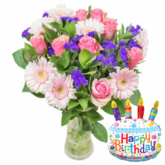 This image captures a joyful birthday arrangement arranged with considered balance and a touch of local heart. At its centre are dozens of soft pink roses, petals layered like silk and shifting from a pale blush outwards to richer pink tones, paired with pale-pink Gerbera daisies that open wide like cheerful faces with muted yellow centres. Interspersed through the larger blooms are sprays of vivid purple filler flowers-statice or limonium-whose fine, clustered texture adds contrast and a carefree, confetti-like rhythm. Deep green, glossy foliage provides a rich backdrop and shapes the silhouette, while stems are visible through a clear glass vase whose slightly widened base shows water and the neat gathering of stems.

To the lower right the composition is playfully anchored by a foil birthday-cake balloon: a white 'frosted' look trimmed with blue piping, scattered multicoloured sprinkles in red, yellow, blue and green, and four striped candles-purple, red, orange and blue-each with a small yellow flame illustration. Across the face of the balloon 'Happy Birthday' appears in bright, varied letters and a tiny 'KALEIDOSCOPE' brand mark sits at the base. As a florist familiar with deliveries across North Watford-whether to Vicarage Road flats or a weekend table by Cassiobury's bandstand-this pairing of classic florals and a playful balloon feels like a perfectly pitched birthday gift: pretty, fragrant and unmistakably celebratory.