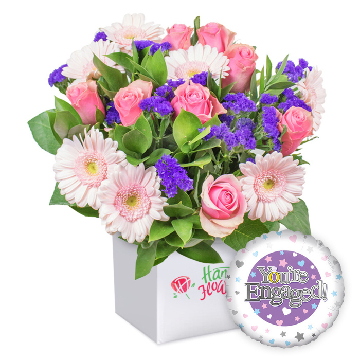 A bright pink and pink-and-white bouquet sits in a square white box, with a small red rose icon on the front and green script, while a glossy foil balloon graces the lower right, its purple disc bearing 'You're Engaged!' in silver and framed by a white ring decorated with pastel hearts and silver stars. The pink roses range from tight buds to opened blossoms, their velvety petals soft under the light, and they mingle with pastel gerberas whose radiating petals are crisp white at the edges and carry pale yellow centers. Deep purple statice punctuate the arrangement, lending jewel-like pops of color, while generous green foliage provides depth and a natural backdrop. The container is a minimal, modern white cube that lets the blooms take center stage, and the whole display exudes a confident, contemporary celebration.

Placed in a North Watford home or office, this design reads as a vibrant yet refined celebration of engagement. It suits both intimate gatherings and larger congratulations, and it travels easily for same-day delivery across the North Watford area, including near Cassiobury Park. The soft pinks, gentle purples, and lush greens convey optimism and joy, while the silver lettering on the balloon adds a touch of glamour that photographs beautifully and preserves the moment for the couple and their loved ones.