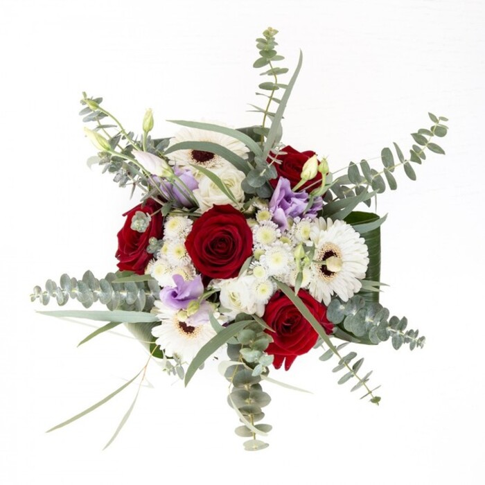 To describe this bouquet as a local florist in North Watford is to appreciate both its elegant confidence and subtle storytelling. Robust, deep red roses spiral out from the center, their forms the embodiment of lasting affection, while snowy white gerberas-petals splayed wide from espresso-dark centers-anchor the composition with classic poise. Wisps of eucalyptus float above, casting delicate shadows reminiscent of sunlight dappled under the oaks lining Radlett Road, lending aromatic freshness and visual movement. Interspersed throughout, gentle lilac lisianthus, some still shy in bud, introduce a pulse of contemporary color-a modern twist befitting North Watford's vibrant character. The bouquet's architecture is underscored by broad, glossy green leaves that curve protectively at its base, offering structural grace and a sense of completeness. Within, clusters of petite white filler blooms evoke the unity and comfort found in close-knit community celebrations. Each element is chosen not only for beauty but also for texture and emotional resonance, the bouquet inviting hands to explore and hearts to reflect. Intended for occasions ranging from anniversaries to housewarmings or tokens of comfort, it embodies both the skill and warmth synonymous with local North Watford florists.