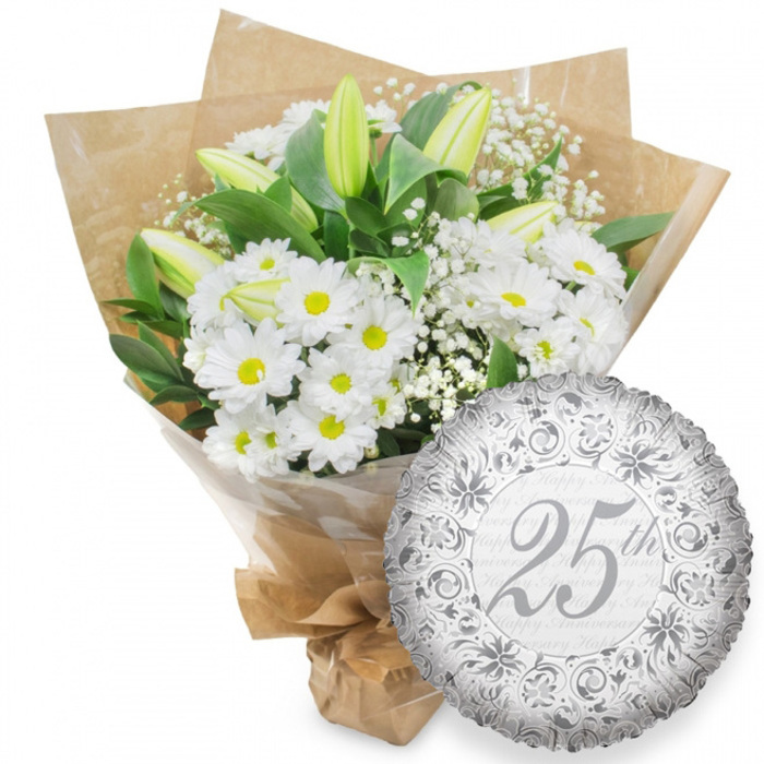 This image shows a classic 25th anniversary display, carefully arranged as if prepared for delivery to a couple in North Watford celebrating a long and steady marriage. On the left, a generous hand-tied bouquet of white flowers dominates the frame, its rounded shape and layered textures giving a sense of abundance without excess. The main blooms are fresh white chrysanthemums with bright yellow centres, each flower neat and symmetrical, creating a field of small, radiant discs. Rising thoughtfully between them are elegant white lily buds, tall and tapering, still closed with a gentle wash of pale green along their outer petals, promising to open over the days following the celebration. Fine sprays of white baby's breath add a misty, romantic haze to the bouquet, threading between the larger heads and softening the lines. Around the outside, deep green foliage spreads in slightly glossy leaves that contrast vividly with the white petals, grounding the composition much as the tree-lined streets around North Watford ground the busy local life. The stems are snugly enveloped in a layer of clear cellophane, then finished in brown kraft paper folded with a rustic, artisan touch, and neatly tied at the base, as if ready to be carried from the florist counter to a doorstep surprise. On the lower right, a single round silver foil balloon leans towards the bouquet. Its shiny, slightly crinkled surface reflects the light and is richly patterned with scrolls and delicate floral motifs in darker silver. At the heart of the design, the inscription 25th appears in flowing script, with a faint, repeated Happy Anniversary in pale grey drifting behind it, leaving no doubt that this is a Silver Anniversary gift ensemble.