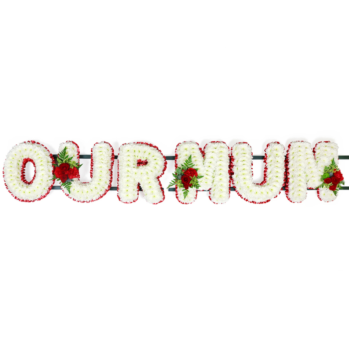 In this image, the words OUR MUM are spelled out in a striking funeral letter tribute, lying horizontally against a bright white background that throws every flower into clear relief. The letters are large and blocky, yet softened by being completely covered in compact white flowers, most likely fresh chrysanthemum heads or similar round-petalled blooms. Their tight placement creates a plush, cushion-like effect, as though each letter has been lovingly padded with petals. Surrounding each letter is a continuous edge of small, deep red blossoms that trace every curve and angle, giving the word a polished, finished look. This vivid red border not only defines the lettering but also symbolises the warmth, strength, and devotion felt for a beloved mother. Behind the flowers, partially concealed, a dark green frame links the letters together, suggesting a solid base suitable for resting on stands at a funeral service or being carried carefully into a chapel in the North Watford area. Nestled along the word are three prominent rose sprays: full-headed red roses clustered with textured greenery, possibly fern and other foliage. One grouping rests between the O and the U, another fills the space between the U and the first M, and the final spray decorates the right-hand end of the last M, providing focal points that catch the eye. These roses add dimension and movement, their velvety petals and rich colour conveying deep affection and remembrance. The overall arrangement feels like the kind of bespoke sympathy tribute a family might commission from Flower Delivery North Watford for a final goodbye at a local church or cemetery, a graceful floral expression of love and thanks.