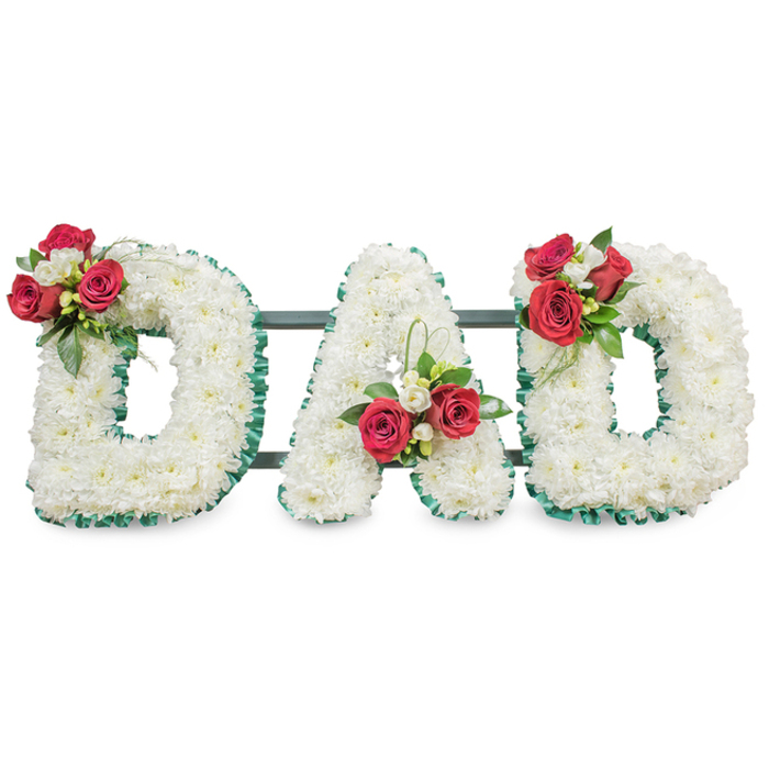 A lovingly crafted sympathy tribute that spells DAD in bold, three-dimensional letters, each letter densely packed with hundreds of pure white chrysanthemum blooms to form a soft, textured expanse of petals. The chrysanthemums' tiny, layered florets give a gentle, cushion-like appearance that reads as both pristine and comforting under soft, even studio illumination. Each letter is edged in a striking emerald-green pleated ribbon which frames the white and lends a thoughtful, tailored finish to the shapes. On the upper left curve of the first D sits an artful grouping of deep red roses in varying stages of bloom, paired with small sprays of white freesia and lush dark-green foliage; the deep red provides an immediate focal point and a sense of enduring love. The central A bears a matching cluster positioned toward its left diagonal, accented by a subtle loop of bright foliage that adds height and movement. The final D mirrors the first with another composed spray of red roses, freesia and leaves, creating a balanced triptych of floral sentiment. Behind the letters, slim dark metal bars are visible, ensuring the display holds its form for presentation at a chapel or outdoor service. Presented on a crisp white background, this arrangement conveys solemnity and remembrance-an ideal, personalised tribute for a father from families in North Watford, delivered with the quiet attention to detail expected by local florists serving the community near Watford High Street and Cassiobury Park.