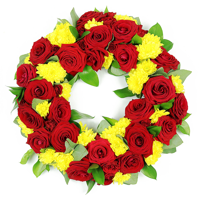 In this image, a substantial circular wreath designed for a funeral or memorial is shown floating against an immaculate white background, the contrast emphasising every detail of its handcrafted design. The wreath itself is a complete, unbroken ring of flowers, composed mainly of luxuriant deep red roses paired with radiant yellow chrysanthemums. Dozens of roses, each one fully opened, form the dominant feature: their tightly layered petals curl inwards and outwards like little velvet cups, displaying a range of red tones from clear crimson to a more sombre burgundy at the centre. Between these roses are bursts of yellow chrysanthemums, their many narrow petals forming cushiony domes that introduce both texture and a feeling of light into the design. These yellow clusters create a gentle rhythm around the ring, brightening the richer, more solemn reds and adding a sense of warmth that suits a celebration-of-life service as much as a traditional funeral in the North Watford area. Underpinning the blooms is a bed of mixed greenery. Broad, healthy leaves with a light sheen provide a dark green base, while occasional stems of paler, slightly bluish foliage - similar to eucalyptus - thread through, giving an airy, delicate touch. The flowers and foliage are packed closely together, so the ring appears full and generous, with a carefully preserved circular opening in the centre that reinforces the symbolism of eternity and enduring love. Neutral, even lighting brings out the vivid colours and subtle shadows, allowing the viewer to appreciate the craftsmanship and care that a local North Watford florist has invested in this thoughtful, respectful tribute.