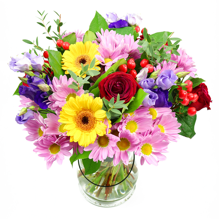 In this photograph, a lavish mixed-colour bouquet stands in a cylindrical clear glass vase, set against a bright white background that lets the flowers take centre stage. The eye is first drawn to the rich, velvety red roses at the core, their petals curled tightly at the centre and soft at the edges, suggesting both passion and tenderness. Just above and beside them, two bold yellow gerbera daisies with dark brown-orange centres open wide like friendly faces, injecting an instant burst of sunshine and joy into the design. Around these main blooms, generous clusters of pink daisies or chrysanthemums create a halo, each small yellow centre surrounded by numerous, finely cut pastel petals that soften the overall effect. Nestled in between, elegant lisianthus in tones of purple and lavender add vertical lines and a cool, sophisticated hue, like gentle brushstrokes of evening sky over the rooftops of North Watford. Here and there, you notice rounded, bright red hypericum berries peeking out between petals, their glossy skins providing a playful contrast to the softness of the flowers. The arrangement is laced with diverse greenery-some leaves deep and broad, others light, slender, and feathery-creating an impression of movement and natural abundance, as though freshly gathered from a well-tended local garden near Garston. The stems are clearly visible through the vase, neatly clipped and immersed in clear water, showing the careful, professional construction of the bouquet. Overall, the display feels celebratory and thoughtful, ideal for sending congratulations, birthday wishes, or a heartfelt thank-you across North Watford, while also working beautifully as a welcoming statement piece in a hallway or on a dining table.