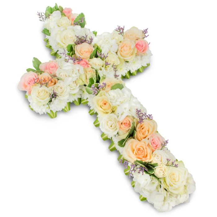 A large, reverent floral cross arrangement fills the frame, photographed cleanly against a crisp white background so that every flower and curve of the design is clearly visible. The cross is densely packed with fresh blossoms, creating a velvety, almost quilted surface in a palette of white, ivory, pale peach, and delicate blush pink. Along the central line and extending into the arms, premium roses take pride of place: generous white and ivory blooms open in graceful spirals, interspersed with soft peach and light pink roses that add gentle warmth and a subtle gradient of colour. Between these focal flowers, abundant white hydrangea heads-or similarly full, cushiony blossoms like chrysanthemums-fill any remaining spaces, building a rich, layered texture that feels both substantial and soothing. Here and there, tiny clusters of lavender or light purple filler flowers are threaded through the design, offering discreet touches of colour that enhance the overall detail without interrupting the calm, pastel theme. Around the outer edges of the cross, fresh green foliage is carefully tucked so that glimpses of leaf tips peek out, framing the floral surface and helping to define the cross's rounded outline. The lighting is soft but bright, casting a faint shadow beneath the piece and adding depth, as though the cross were gently resting above the background rather than on it. This kind of floral tribute, crafted with such precision and tenderness, is typical of what families in North Watford might choose for a funeral, memorial service, or church altar display, capturing both deep faith and a respectful, enduring remembrance. It suggests a design created by a local florist who understands the quiet dignity needed for final farewells in and around the North Watford community.