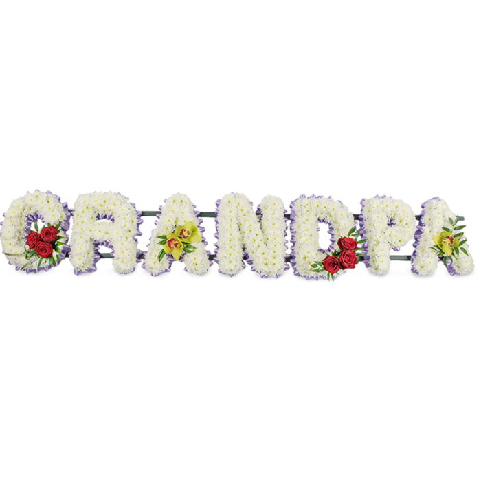This photograph shows a lovingly crafted funeral tribute that spells out GRANDPA in strong, upright capital letters, arranged in a straight line against a simple white backdrop so that only the flowers speak. Every letter is built from dense clusters of small white chrysanthemums, their rounded petals layered so closely that the surface appears soft and pillowy, as though each letter could gently cradle a memory. Around the outer edge of the flowers, a very fine trim of pale lavender-purple ribbon or pleated fabric runs continuously, lending each letter a delicate outline that sharpens their shape while maintaining a peaceful, understated look. In the opening G, tucked into the curve of the letter, sits a compact spray of three to four deep red roses surrounded by glossy green foliage, acting as a rich focal point that symbolises deep affection and gratitude. The third letter, A, carries a refined accent of yellow-green orchids with touches of reddish-brown in their centres, their elegant, slightly exotic blooms hinting at a grandfather's individuality and grace. At the heart of the tribute, the D echoes the G with another neat cluster of red roses and greenery, and the final A repeats the orchid detail, bringing balance and continuity to the design. Discreet horizontal bars, finished in a darker tone, support the letters and keep them aligned while remaining unobtrusive. The overall mood is tranquil, respectful, and deeply personal, the sort of floral lettering a North Watford family might place beside the coffin at a local church or cemetery service, honouring a much-loved grandad with purity, peace, and lasting remembrance.