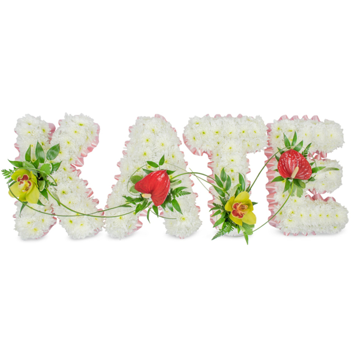 This image shows a handcrafted funeral flower tribute presenting the name KATE in four large capital letters, laid out in a clean line against a simple white background so that every bloom is clearly defined. Each letter is built from a dense covering of white chrysanthemums, their small, rounded petals overlapping to form a plush, even surface reminiscent of soft fabric. The edges of the letters are trimmed with a neat band of light pink satin ribbon, the gentle colour adding a whisper of sweetness and softening the strong, block-style shapes. Set into the white floral base are carefully placed clusters of greenery and striking focal flowers that give character and meaning to the tribute. On the K and T, yellow-green cymbidium orchids with distinct reddish-brown markings at their centres introduce a refined, almost regal note, while their firm, waxy petals lend contrast to the feathery chrysanthemums. A single red, heart-shaped anthurium decorates both the A and the E, its high-gloss surface reflecting the light and creating a bold symbol of love and remembrance. Between the letters, slender green vines and tendrils arc and curl, visually linking the entire name and suggesting continuity and connection even in times of loss. The overall feel is peaceful, dignified, and deeply personal, the kind of custom name tribute families in North Watford might send to honour a loved one at a funeral service, local church, or cemetery. Carefully arranged by an experienced florist, this piece reflects the quiet elegance and thoughtful craftsmanship often sought for sympathy flowers and memorial deliveries in the North Watford community.