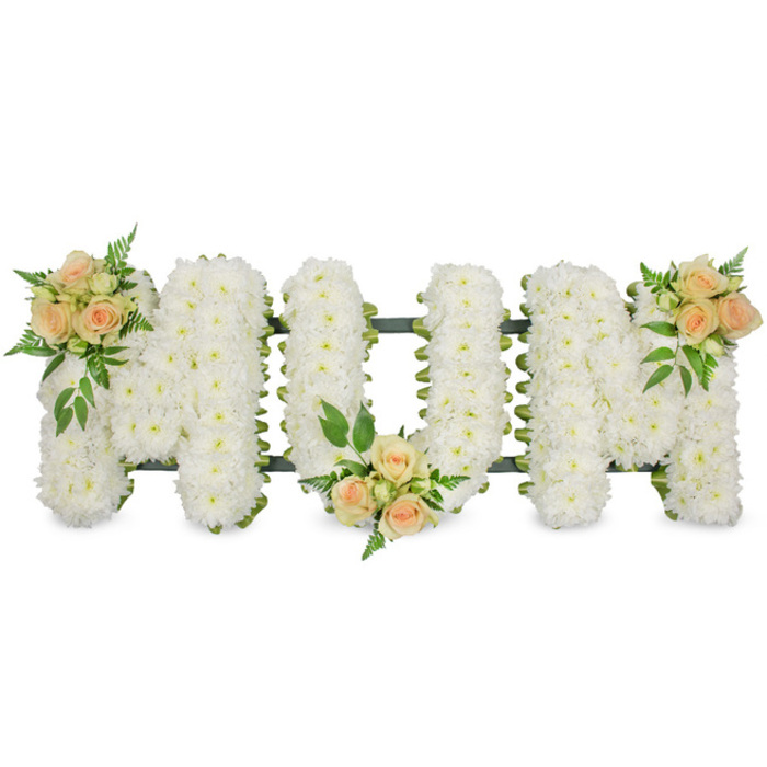 A refined floral tribute forms the word MUM in bold, upright block letters, designed as a centrepiece for a funeral or celebration of life in the North Watford area. Each letter is completely coated in small, pristine white chrysanthemums, set so closely together that no gaps are visible. The mass of white petals creates a velvety, almost pillow-like texture, suggesting softness and purity, while the rounded flower heads give a gentle, comforting look from every angle. A narrow outline of dark green ribbon and supportive foliage traces the edges of the letters, defining their clean shape and hinting at the strong framework beneath the blooms. Three floral accents of roses in soft peach and blush pink bring warmth and personality. On the first M, a cluster of roses is placed at the top left arm; on the U, a matching cluster nestles at the bottom centre; and on the second M, another sits at the top right arm, echoing the first and completing the composition. Each cluster combines open rose heads with smaller buds, surrounded by glossy dark leaves and feathery green fronds that give the design movement and a natural garden feel. Set against a bright white background, the tribute looks calm, luminous, and thoughtfully composed, ready to be displayed at a service near Garston or along St Albans Road. The contrast of white chrysanthemums and peach roses conveys deep affection, remembrance, and gratitude for a beloved mother, capturing both the gentleness and strength of her presence.