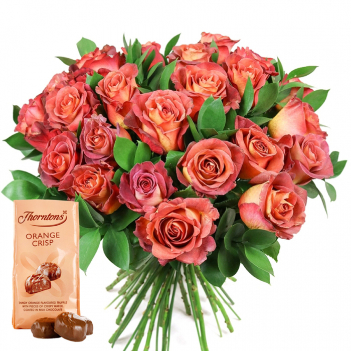 Central to this elegantly composed North Watford scene is a lush, full bouquet of roses, its colours shifting with natural artistry from hues of peach and golden orange to rich coral, pink, and deeper reddish tones. The rounded arrangement, meticulously crafted by local florists, is a marvel of contrasts and harmony-each fresh rose densely petalled, some revealing subtle bi-colour transitions, others awash with creamy centres and sun-kissed edges. Abundant green foliage, carefully selected for depth and texture, weaves through the display, its vibrant tones enhancing the warmth of the blossoms and echoing the green spaces beloved in the North Watford area. In the corner of the composition sits a light cream pouch of Thorntons Orange Crisp chocolates, marked clearly with brand and product names. The inviting illustration beneath the text hints at the velvety, citrus truffles nestled inside, while two unwrapped chocolates, darkly glossy and perfectly rounded, rest temptingly before the bag. The arrangement's visible green stems suggest recent cutting, reaffirming the bouquet's freshness and the skilled hands behind its preparation. The white background ensures nothing distracts from the splendour of roses and the gourmet allure of chocolates. Altogether, this gift set expresses both celebration and appreciation, making it a thoughtful choice for local occasions such as Mother's Day, anniversaries, or birthdays in North Watford. It seamlessly blends the senses-visual, tactile, and gustatory-into a vivid tribute to life's most heartfelt moments.