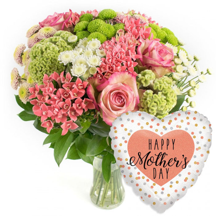 A colourful Mother's Day bouquet with coordinating balloon is photographed in crisp, even light against a plain white background, as though ready to feature on a North Watford flower delivery page. The flowers are arranged in a simple clear glass vase, the stems visible and neatly trimmed, with the water line subtly catching the light. Rising from the vase is a generous, rounded mass of blooms, carefully composed so that every angle feels full and lush. The arrangement is dominated by large, graceful pink roses; their petals display a romantic gradient, moving from slightly deeper rose in the centre to softer, almost pearly pink at the outer edges, like a gentle blush. Interwoven among them are clusters of coral-pink blooms reminiscent of kalanchoe or spiky spray flowers, adding depth and warmth. Vivid lime-green button chrysanthemums and fluffy chartreuse florets introduce a modern flourish, their compact round heads and frilled textures standing out against the smoother rose petals. Here and there, small white daisy-like chrysanthemums light up the bouquet, their bright faces giving an airy, uplifting feel. Rich green foliage forms a dense base, framing the colours and making the whole piece look fresh, as if it has just been prepared in a North Watford studio close to the High Street. To the right of the bouquet, slightly overlapping its base, a shiny heart-shaped foil balloon completes the gift. The balloon has a predominantly white and silvery background dotted with playful specks of gold, silver, and coral-peach, while a larger peach heart in the centre holds the message HAPPY Mother's DAY in smart black lettering. The overall mood is festive and affectionate, evoking the joy of sending a complete Mother's Day surprise to a mum in North Watford, perhaps overlooking the green spaces near Garston Park.