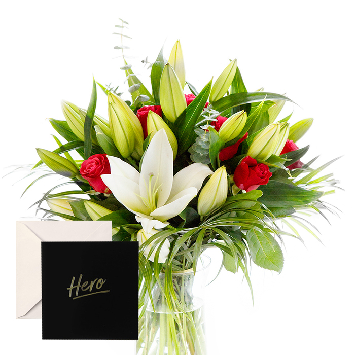 As a florist, there is joy in blending bold with serene, and this arrangement embodies that harmony for North Watford. The white lilies drift at the heart of the bouquet, luminous and airy, their satin petals contrasting splendidly with the tactile, lush greenery that encircles them. Rich red roses punctuate the design, each bloom a symbol of love and respect. The verdant leaves provide a cooling, forest-like backdrop, while unopened lily buds suggest anticipation and new beginnings. In soft natural light, the bouquet feels alive and uplifting, perfect for honouring a strong performance or celebrating a significant achievement. The accompanying Hero card makes this gesture feel intimate and enduring, a quiet vow of admiration carried with beauty, and delivered with care to a door near Market Street or Cassiobury Park.

The arrangement stands in a clear vase, allowing the stems to telescope upward in graceful order while the surrounding greenery frames the blooms like a living sculpture. It travels well for North Watford occasions, from graduation celebrations to workplace acknowledgments, bringing a sense of calm confidence to the room. For same-day delivery across the area, freshness travels quickly, carrying scent and emotion to the doorstep with reliability. The craftsman's touch is evident in every fold of tissue and ribbon, a local florist's pride on display in the North Watford community.