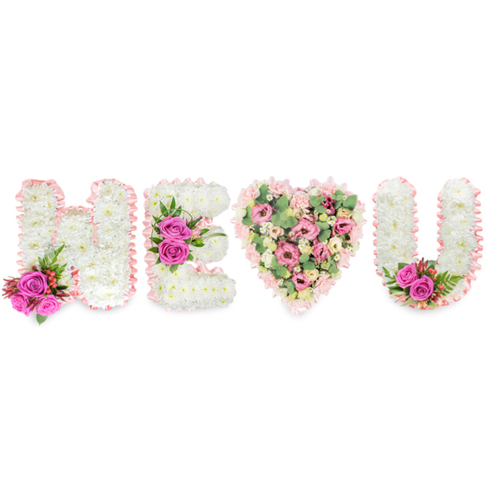 Set against a pristine white field, this floral composition spells out H, E, a heart, and U - a quiet, intimate message fashioned from classic sympathy and romantic flowers. The three letters are formed from compact beds of white chrysanthemum heads, each bloom packed so closely that the letter surfaces appear like soft white cushions. A pale blush satin ribbon trims the perimeter of every letter, its subtle sheen catching soft light and lending a gentle, almost ceremonial edge. Each letter is balanced with a colourful accent of fuchsia-pink roses: one accent cluster sits at the lower left of the H among slender deep-green, fern-like foliage and tiny berry clusters; another set brightens the middle bar of the E; and a matching pair adorn the lower inside curve of the U. Between the E and the U, a generous heart shape becomes the focal pause - composed of layers of soft pink carnations and delicate lisianthus or small roses in creamy blush tones, cushioned and intertwined with pale green eucalyptus leaves. The eucalyptus contributes a cool, herbal scent and a muted green wash that keeps the heart tender rather than sugary. The arrangement is captured in even daylight that reveals the texture of petals and ribbons without dramatic shadow, offering a calm, respectful presence suitable for funeral services, anniversaries of remembrance, or a deeply personal declaration of love. As a piece that would resonate with families across North Watford - from homes near Watford Junction to quiet streets off Hempstead Road - it reads as an expert florist's expression of care, memory and ongoing affection.