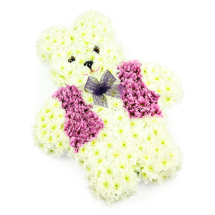 A charming teddy bear-shaped floral arrangement sits against a simple white backdrop, created entirely from fresh flowers that seem to radiate softness and care. The bear's body is sculpted from numerous small, tightly packed white and pale cream chrysanthemums, each bloom placed so precisely that the entire figure appears smooth and cuddly, like plush fabric rendered in petals. The rounded head, pronounced ears, and plump arms and legs are all defined by gentle contours and subtle shading within the blooms, giving the bear a three-dimensional, lifelike presence. Its face is brought to life with two dark, button-style eyes that lend a tender, almost storybook expression, while a tiny black triangular nose anchors the centre. Just beneath, a faint suggestion of a smile can be seen, implied by the curved positioning of the surrounding petals, adding a note of quiet reassurance. Across the bear's chest, a neat floral waistcoat is fashioned from deep pink and mauve-toned flowers, likely hydrangea or chrysanthemum heads grouped together to form a rich band of colour. This vest frames a delicate bow of sheer violet netting at the neckline, the translucent fabric adding a whimsical, slightly formal touch, like a little party outfit prepared with love. The neutral background and even lighting allow the intricate textures and soft pastel tones to stand out clearly. This teddy tribute, the kind of bespoke piece Flower Delivery North Watford might prepare for families in areas such as Courtlands, Oxhey, or along North Western Avenue, is ideal for a child's funeral, memorial, or christening reception, offering a floral embrace that symbolises innocence, remembrance, and enduring affection.