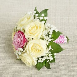 Imagine receiving a petite bouquet that captures the gentle poetry of North Watford's blooming gardens-a composition of creamy ivory roses nestled together, their silken petals unfolding with tranquil grace. Cloudlike clusters of baby's breath weave an ethereal border, lending a sense of softness and openness that whispers of joyful beginnings. In the midst of these pale blooms, a single, radiant magenta-pink rose beams with heartfelt exuberance, evoking the vibrant colours found in the spring displays at local woodlands or the edge of Callowland Park. Each open rose and sprig of foliage glows under soft, diffused light, as if kissed by the early morning. The bouquet's handle is lovingly bound by smooth, bright pink satin ribbon and adorned with a strand of luminous pearls, spiralling down in a modern twist on classic bridal design. The gentle hues and tactile details-velvety blooms, cool pearls, fresh greenery-meld to create an uplifting, tender mood, perfect for weddings, anniversaries, or heartfelt North Watford celebrations. The bouquet exudes a timeless romance-its delicate fragrance hinting at hidden garden corners and cherished moments, while its vibrant craftsmanship reflects the care and expertise of a local florist deeply rooted in the community. This is more than a bouquet; it's a carefully-arranged symbol of joy, ready to be carried down an aisle or gifted to mark a special occasion, its elegance and emotion woven into every detail.