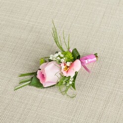 Evoking the gentle spirit of North Watford in springtime, this exquisite boutonniere is a composition where every petal and leaf speaks to the artistry of local floristry. The central focus is a blushing rose in soothing pastel pink, its tightly layered petals forming a perfect spiral of freshness. Next to the rose sits a smaller, peach-tinted bloom-perhaps Alstroemeria or lisianthus-its petals unfurling with subtle streaks of yellow and fine, natural markings at the center, a reminder of the intricate wildflowers blooming along local avenues. Romantic clusters of feathery baby's breath add a cloud-like note, while miniature, green chrysanthemums introduce a lively textural counterpoint. Surrounding foliage includes wisps of delicate grass and finely textured fern, complimented by lush, deep green leaves-one cleverly folded to frame the rose. All elements are gathered and secured with a satin-finished, fuchsia pink ribbon tied in a neat, celebratory bow, bringing a sophisticated pop of colour against the soft, woven linen background. This elegant buttonhole is ideal for grooms, groomsmen, or special wedding guests wishing to embody understated Watford elegance and flair. Each fragrant bloom is carefully chosen and arranged with the thoughtful expertise characteristic of North Watford's thriving floral community, ensuring this piece is both visually stunning and locally inspired.
