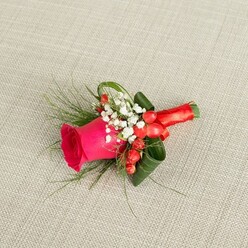 A richly detailed boutonniere is presented on a softly woven, light beige fabric that resembles natural linen, its gentle texture creating a calm backdrop like a quiet table laid for a wedding morning in North Watford. At the center sits a confident fuchsia rose, its petals deeply furled at the core and gradually unfolding in plush, velvety layers, the hot pink tone glowing warmly as if just opened from a fresh delivery. Nestled around the base of this rose are clusters of tiny white baby's breath, their countless miniature blooms forming a frothy halo that softens the vivid central flower and suggests innocence and tenderness. Threaded between the whites and pinks, glossy scarlet hypericum berries add bright, rounded accents, their lacquered skins catching the light and lending a subtle festive note, perfect for winter weddings or Christmas parties near Garston or Nascot Wood. Slender, fern-like fronds reach out in airy green arcs, contrasting with broader, darker leaves that are artfully curled and tucked to give structure and depth, much as a skilled local florist would build up texture in a hand-tied buttonhole. The stems are bound together with a rich red satin ribbon, wrapped smoothly and finished with a neat, elegant bow that balances comfort on the lapel with a sense of quiet luxury. Viewed from slightly above, every detail-the tight spiral of rose petals, the soft cloud of gypsophila, the polished berries, and the gleam of ribbon-shows an expertly composed floral accessory ready for a groom, groomsman, or prom guest stepping out along St Albans Road.