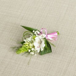 An elegant, compact boutonniere is presented on a pale, linen-textured fabric that looks like softly woven beige cloth, its subtle weave giving the scene a warm, natural feel. Centred in the arrangement is a pristine white alstroemeria, also known as a Peruvian lily, its petals gently curling outward and displaying fine reddish-brown streaks near the throat, like delicate brushstrokes painted by hand. Nestled to the left of this focal bloom is a bright, conical cluster of lime-green buds, likely Ornithogalum, packed tightly together to form a sleek spike that brings a contemporary edge and intriguing texture. Tiny white baby's breath blossoms are scattered throughout, their airy, cloud-like sprigs lightening the whole piece and lending a dreamy, romantic softness, as if the boutonniere were made for a quiet ceremony at a registry office near North Watford's St Albans Road. Rich green foliage frames the flowers: broader, pointed leaves offer structure and depth, while slender, grass-like tendrils curve and twist with grace, adding a sense of motion that keeps the design from feeling static. At the right-hand side, the stems are carefully wrapped and cinched with a gleaming pink satin ribbon, tied into a petite, symmetrical bow that introduces a fresh, joyful accent of colour. The lighting is even and gentle, bringing out the delicate textures of each petal, bud, and leaf, and emphasizing the skilled workmanship behind this small yet meaningful floral accessory, ideal for a groom, prom date, or guest at a celebration anywhere across North Watford.