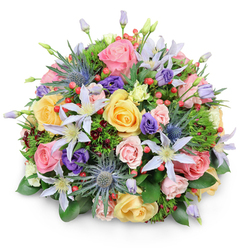A rounded, luxuriously full bouquet sits against a crisp white backdrop, the pristine setting drawing attention to each petal, stem, and berry in the composition. The arrangement is tightly domed, almost like a blooming hedge captured at the height of spring in a North Watford garden, its surface rippling with roses in pastel pink, warm yellow, and creamy peach. Some roses are wide open, their spiralling centers exposed, while others remain more modest and half-open, suggesting movement and time. Between these classic flowers, delicate clematis in white and pale lavender stretch out in starry shapes, their slim petals and golden centers bringing an airy, climbing-vine energy to the design. Blue eryngium, with its firm, thistle-like heads and collar of sharp, metallic blue-grey bracts, punctuates the softness, standing almost like tiny sculptures and lending a slightly wild sophistication. Nestled among them are purple lisianthus in varied stages of bloom, from tightly furled buds to softly opening cups, adding depth and a velvety richness of colour. Bright red hypericum berries appear in small clusters, their round, bead-like forms creating playful bursts of colour that echo the warmth of a celebratory moment. Lush greenery frames and supports the bouquet, combining broad, lacquered leaves, delicate fern-like sprigs, and a few darker, burgundy-tinged leaves that provide shadow and nuance. The lighting feels gentle and even, the kind you might notice through a window on a calm morning in North Watford, perhaps near Garston Park. It is an arrangement that suggests joy, gratitude, and thoughtful care, ideal as a centerpiece on a family dining table or a surprise delivery to brighten a quiet townhouse along North Western Avenue.