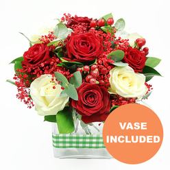 This image showcases a romantic red and white rose bouquet that feels perfectly suited to a cosy North Watford dining room or a smart office just off St Albans Road. The composition is carefully balanced: sumptuous deep red roses sit alongside creamy white roses, each bloom open enough to show its swirling heart of petals, yet still fresh and full of life. Threaded between the roses are airy clusters of tiny, bright red filler flowers, similar to dyed gypsophila, which soften the overall outline and give the arrangement a lightly frosted, celebratory look. Glossy red hypericum berries, rounded and smooth, add texture and a playful sparkle, as though tiny cherries have been tucked among the blossoms. The foliage is rich and varied, with deep green leaves and elegant stems of eucalyptus adding a whisper of silvery tone that cools and complements the warm reds. All of this is gathered into a sleek, clear rectangular glass vase, its transparency revealing the stems and water inside and grounding the design with a simple, modern base. Around the centre of the vase runs a green and white gingham ribbon, its checked pattern evoking rustic kitchens, country fairs, and the relaxed charm of local markets near North Watford. At the bottom right corner of the photograph, a bright orange circular label reads "VASE INCLUDED" in bold white letters, drawing the eye and confirming that the gift is complete and ready to display the moment it is delivered. The mood is joyful yet refined, perfectly suited for birthdays, romantic surprises, or a special thank-you gesture sent within the local area.