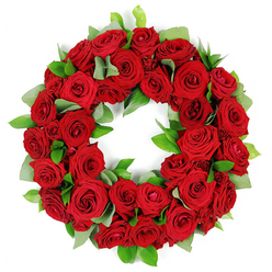 In a moment of respectful ceremony, this circular wreath of red roses feels crafted by careful hands and thoughtful memory. Resting against a clean white backdrop, the wreath gathers dozens of blooms in varying stages of bloom, from snug buds to fully opened, velvety petals rich in color. The crimson surface is lush and luminous, with light catching the edges and revealing subtle tonal shifts that deepen toward burgundy at the center. Through the ring, wisps of soft green foliage peek-broad, matte leaves akin to eucalyptus and sleeker, glossy ruscus-adding breath and texture to the sea of red. The circle is perfect and unbroken, a symbol of everlasting connection and remembrance. The arrangement radiates a dignified calm, a mood well suited to sympathy, funerals, or anniversaries. The crisp white background gives the arrangement a ceremonial presence, letting every contour and petal define its place in the design. Local readers in North Watford will recognise the piece as the voice of a trusted florist, one that speaks of care, of freshness, and of reliable delivery. This wreath, balanced with craft and restraint, travels beautifully to venues around town, with same day or next day delivery across the North Watford area to support families in their moments of reflection and memory.