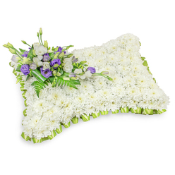 This rectangular floral pillow is an expression of careful sympathy, assembled from a dense field of hundreds of immaculate white chrysanthemum heads that create a lush, uniform surface reminiscent of a soft, sleeping cushion. The petals read as a serene white landscape, while a pleated band of pale green ribbon traces the entire edge in precise loops, lending a delicate, fresh contrast that defines the shape and offers a hint of renewal. Against a pristine white background and under soft studio light, the pillow's puffy profile and faint shadow become an object of calm focus, each chrysanthemum contributing to an overall impression of peace and dignity.

At the top-left corner a small, elegant spray of accents draws the eye: white lisianthus with their soft, layered petals are paired with richly hued purple lisianthus-some opening, some tenderly furled-to introduce a respectful, comforting colour note. Feathery fern fronds and glossy dark green leaves weave through the cluster, and a broader green leaf wrap secures the stems, giving the accent a composed, refined finish. The scent is quietly floral rather than sweet, and the arrangement's texture invites a gentle, reverent touch. Prepared with the care expected in North Watford, this tribute is the sort of memorial piece Flower Delivery North Watford would ready for a funeral or graveside service near Watford High Street or Vicarage Road, offering a sincere, floral language of condolence.