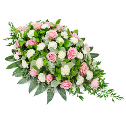 A large, elongated teardrop funeral spray is photographed against a clean white backdrop, its soft pink and white flowers arranged with the kind of care you might expect from a long-established North Watford florist. The upper left of the composition is densely filled with blush and rose-pink roses, some still cupped like shy buds, others fully open to reveal their intricate, layered hearts. Interwoven among them are pristine white carnations and small spray carnations, their frilled petals forming a gentle, cloud-like texture that softens the entire arrangement. The blossoms sit on a lush bed of mixed greenery: broad, glossy dark green leaves give the piece structure and weight, while rounded, silvery eucalyptus leaves introduce a cooler, misty tone and a sense of tranquillity. Along the tapering right edge, trailing strands of deep green ruscus extend outward, shifting the teardrop into a flowing, almost river-like form that suggests the passage of time and the continuity of love. The spray appears full yet not overcrowded, with every flower given space to be seen, as if laid lovingly across a casket or displayed beside a memorial picture. Soft, even lighting ensures that every hue-from the pale blush petals to the inky green foliage-is clearly visible. The overall mood is reflective and soothing, echoing the quiet paths of North Watford's local cemeteries and churches, and offering a respectful, beautiful way to say goodbye when words alone feel insufficient.
