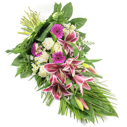 Set against a clean white background, this refined sympathy spray stretches diagonally from top left to bottom right, creating a gentle crescent shape that feels both flowing and composed. At its centre, dramatic Stargazer lilies in vivid fuchsia-pink command attention, their wide petals rimmed in white and sprinkled with dark burgundy speckles, capturing that blend of emotion and gravitas that suits a final farewell. Some lily buds remain elongated and closed, blushed with pink and green, suggesting memories still cherished. Nestled beside them, bright magenta gerbera daisies provide lively, round bursts of colour, balanced by clusters of elegant white roses whose tightly rolled petals speak of respect and tenderness. Soft white carnations add a cloud-like texture, their ruffled petals creating a gentle cushion around the bolder blooms. Tiny white daisy-style flowers thread through the design, softening edges and adding delicate detail. A tapestry of greenery supports the flowers: broad, dark leaves anchor the top, airy fern fronds bring a natural, woodland texture, and long, slender foliage arcs toward the lower right, enhancing the elongated silhouette. The bound stems at the upper left clearly show this is a hand-crafted sheaf, carefully composed by an experienced florist who understands the quiet formality needed for funerals and memorials. The arrangement feels peaceful and consoling, suitable for honouring a loved one at a service in North Watford, from local churches to crematorium chapels, or for sending heartfelt condolences to families living around Garston, Nascot Wood, and nearby streets.