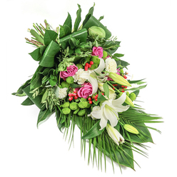 There's a gentle poetry woven through this elongated floral spray, a signature touch of North Watford's floristry scene. The arrangement is an artful blend of purity, hope, and respectful tribute, designed with a sweep of white oriental lilies-some at their peak bloom, exposing powdery golden stamens, others in quiet bud. Nestled amidst the lilies, clusters of rich pink and fuchsia roses add a comforting embrace, their tones deepening the atmosphere with memories and love. The interplay of smaller, ruffled white spray carnations and unexpected button-like green santini chrysanthemums creates both texture and visual intrigue-the green adds moments of brightness reminiscent of the springy lawns of Cassiobury Park. Red hypericum berries, scattered like small jewels, provide cheerful punctuation throughout the canvas of dense, verdant foliage. This base, constructed from glossy dark green leaves-some elegantly folded, some feathery and light, others trailing like fronds-echoes the wildness and structure of gardens that flourish in North Watford. Under gentle, natural light, each bloom and berry casts soft shadows, inviting both reflection and peace. The final impression is one of both grandeur and gentleness: a piece that would comfort at a time of farewell, its every element thoughtfully chosen to honour memory and offer serene beauty within the local context.