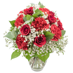 A rich, rounded bouquet of red and white blooms is displayed in a clear glass vase, its shape full and abundant, set cleanly against a bright white backdrop that lets the flowers take centre stage. Deep crimson red roses, with their tightly layered, velvety petals, form the romantic core of the arrangement, each bloom curling inward in graceful spirals that evoke classic love stories and heartfelt confessions. Between them, plump red carnations, intricately ruffled and densely petalled, create a sense of softness and volume, their slightly varied shades of crimson and scarlet giving subtle movement to the eye. Soft clouds of white baby's breath drift through the bouquet, filling any spaces with tiny, star-like blossoms that seem to float among the bolder flowers and bring a fresh, airy lightness. Nestled among the blooms is a mix of lush greenery, from the deeper green of the rose leaves to more muted, rounded eucalyptus foliage, adding layered tones of green that enhance the reds and whites without overpowering them. The clear vase, with a gently widening neck and a sturdy base, holds the stems in clean water, their cut ends neatly aligned, reflecting the meticulous care a North Watford florist might take when preparing a gift for delivery along St Albans Road or near Cassiobury. Bright studio lighting highlights the natural sheen on the petals and the crisp edges of the carnations, creating a look that is both festive and refined. This bouquet feels perfect for anniversaries, Valentine's surprises, or simply sending love and appreciation to someone special in North Watford.
