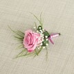 A single blush pink rose boutonniere lies carefully arranged on a softly textured, light beige linen cloth, the kind of natural fabric you might see on a rustic table in a North Watford townhouse near Cassiobury Park. The rose is semi-open, its velvety petals spiralling gently from a pale, almost shell-pink centre to a slightly deeper, romantic pink at the curled outer edges, suggesting perfect freshness and a tender, unfolding moment. Tiny clusters of creamy white baby's breath nestle closely around the base of the bloom, each minute blossom like a bead of soft light, adding a cloud-like halo that makes the rose appear even more luxurious and full. Fine, emerald green, grass-like foliage fans out delicately from behind, creating a light, airy frame, while a broader, deeper green leaf is folded neatly to cradle the stems and give the composition a tailored, polished line that would sit beautifully on a lapel during a wedding at a local North Watford venue or a prom at a nearby school. The stems are bound with a lustrous ribbon in complementary tones of lavender-pink and rich magenta-purple, wrapped smoothly and tied in a simple, secure knot that adds a modern, sophisticated touch without overpowering the flowers. Soft, even lighting glides across the scene, picking up the texture of the woven linen and the subtle sheen of the satin, while gentle shadows lend depth and a three-dimensional feel, as though you could reach out and pin the boutonniere onto a jacket. This image evokes quiet romance and thoughtful craftsmanship, perfectly suited to illustrate elegant wedding flowers, groomsmen accessories, or lapel blooms available for same-day delivery across North Watford and the surrounding streets.