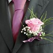 This boutonniere perfectly captures the delicate poetry of North Watford celebrations, its every detail infused with artistry and emotion. At its center, a freshly opened blush-pink rose sits in quiet splendour, its satin petals unfurling in soft layers that almost imperceptibly shift from pale pink to a deeper rose, as if lit by the glow of a Watford sunrise. The sweet, understated fragrance seems to promise hope and new beginnings-ideal for weddings, proms, or milestones shared with loved ones. Gentle halos of baby's breath envelop the rose, their frothy white petals lending a touch of ethereal lightness, while subtle sprays of green foliage provide balance and evoke local woodlands. Secured in place by a shimmering lilac satin ribbon, the boutonniere is crafted with a florist's eye for harmony and nuance. Resting against a crisp, dark charcoal suit jacket, the vivid magenta-pink tie at the wearer's neck completes the carefully layered palette, each element chosen to radiate modern elegance with timeless charm. For those in North Watford seeking floristry that turns a small accent into a cherished symbol of joy, this piece is a reminder that every celebration deserves thoughtful artistry and a touch of local flair.