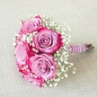 A vibrant and romantic bridal or bridesmaid bouquet, expertly arranged by a North Watford florist, features five lush roses whose petals dance from soft lavender hearts to vivid magenta edges. Each rose is surrounded by tender tufts of white baby's breath, which weave delicately through the bouquet, creating a visual impression of airy lightness and spring. The neatly gathered stems are wrapped in a plush, deep purple satin ribbon, spiral-bound with iridescent pearl strands that add a touch of luxury and gentle shimmer, just right for Watford celebrations. At the handle's end, freshly cut green-brown stems peek out beneath the elegant wrapping, offering a rustic contrast to the bouquet's overall polish. The arrangement, lying softly atop a warm beige textile surface-perhaps echoing linens found in homes along St Albans Road-draws the eye with its vivid colours and refined textures. Thoughtfully designed for North Watford occasions, this bouquet symbolizes both joyful romance and sophisticated style, making it a fitting visual inspiration for wedding features, local bridal events, or heartfelt anniversary surprises within the community.