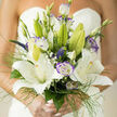 A refined bridal bouquet arranged with quiet confidence: large, star-shaped white lilies take center stage, their velvety petals unfolding in broad, pure sweeps that catch the light with a soft sheen. Interspersed among them are lisianthus blooms, each rimmed with a whisper of purple that deepens the whites and adds a gentle, modern edge. Slim veronica spikes and tiny baby's breath clusters thread through the design, their fine textures and miniature blooms bringing delicate punctuation and an airy, handcrafted feel. Slender green grasses and feathery foliage form a loose frame, giving movement and lift so the bouquet reads as both romantic and effortless.

The fragrance is quietly intoxicating - a honeyed lily sweetness rounded by fresh green notes - conjuring the kind of soft morning light you might find on a walk from Watford Junction toward Cassiobury Park. Each stem is chosen and placed to balance shape and scent; buds and open flowers alternate so the bouquet promises longevity and evolving beauty across the day. This composition speaks of classic ceremony refined for contemporary tastes: graceful, tactile, and intimate. Prepared with the skill of a local florist who knows North Watford's wedding venues and the rhythm of community celebrations, it carries an emotion of gentle anticipation and tasteful celebration, suited for both a small family gathering and a larger, elegant affair.
