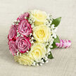 Laid gently on a pale, woven surface that resembles fine hessian in a warm oatmeal shade, this classic hand-tied bouquet has the balanced elegance of a well-loved wedding photograph. From above, you can clearly see the circle divided into two harmonious halves: one side a rich sweep of magenta-pink roses, the other a soothing cluster of soft, buttery yellow blooms. Each rose is at its peak, with layered petals curling outward in perfect spirals, giving the arrangement a plush, almost velvety texture you can imagine brushing with your fingertips. Dotted throughout, delicate sprigs of white gypsophila create a lacy network of tiny blossoms, lightening the composition and adding that airy, traditional detail so many brides in North Watford still ask for. A few dark green leaves peek modestly from beneath the flowers, framing the design without ever stealing focus. The stems below are drawn tightly together and wrapped in gleaming pink satin ribbon, smooth and lustrous, as if waiting to be held on a walk from a church near Garston or a registry office in central Watford. Around the ribbon, a slender garland of white pearls winds in a gentle spiral, catching the light and echoing the classic bridal jewellery so often worn nearby. The overall mood is soft and romantic, with an imagined scent of fresh roses drifting through the air, making this bouquet perfect for wedding photography, anniversary surprises, or a proposal planned with same-day delivery across North Watford.
