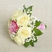 A small, elegant bouquet lies on a pale, woven linen fabric, bathed in the soft daylight typical of North Watford mornings. The arrangement radiates quiet romance, anchored by five creamy ivory roses whose unfurling petals create a lush, textural centrepiece. Offset among them is a single deep magenta rose, its bold hue reminiscent of vibrant spring blossoms in local Watford parks. Scattered through the bouquet, airy clusters of white baby's breath lend a light, classic touch, while a handful of deep green leaves peek from between the blooms, offering a subtle, grounding contrast. The stems are gathered and wrapped with a bright pink satin ribbon, the handle adorned by a spiral of gleaming white pearls-a nod to both tradition and modern elegance. The ambient lighting enhances every curve and detail, from the satiny petals to the soft shine of the ribbon and pearls. This bouquet feels fresh and timeless, an ideal accent for North Watford weddings, bridal parties, or any celebration marked by love and understated sophistication. Its gentle fragrance and tactile richness evoke the spirit of local floristry-effortlessly graceful, thoughtful, and perfectly in tune with the joyful energy of the community.