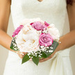 This bridal bouquet captures the calm, romantic side of a North Watford wedding, as if it has just been lifted from a sunlit dressing table by a bride preparing to walk down the aisle. At its core are grand, creamy peonies, petals unfolding in layers of ivory and soft vanilla, each bloom round and full like a gentle cloud resting in her hands. Nestled between them are roses in cool dusty pink and faint violet, the colours reminiscent of evening skies over Callowland Recreation Ground, bringing a subtle depth and movement to the design. Specks of airy gypsophila peek out from between the larger flowers, forming delicate clouds that lend a classic bridal lightness, almost like a soft breath of mist around the bouquet. A collar of rich green foliage surrounds the flowers, leaves with a smooth, slightly waxy texture that keeps the arrangement looking fresh and structured, as if ready to be carried from the ceremony to a celebration near North Watford's familiar streets. The overall shape is neat and compact, perfect for an intimate grasp, with stems gathered tightly enough to feel secure yet still natural. In the soft natural light that often filters through local registry offices and village halls, the colours appear gentle but assured, reflecting harmony, grace, and quiet joy. It is the kind of bouquet that suggests careful thought and heartfelt intention, ideal for a couple wanting their flowers to mirror the warmth and tranquillity of their day in and around North Watford.