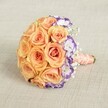 Displayed on a muted beige textile, this beautifully composed bridal bouquet features an exuberant gathering of warm peach and soft coral roses at its centre-each bloom flawlessly open and full, lending a lush, inviting texture typical of North Watford's finest wedding floristry. On one side, white lisianthus blossoms edged with violet and plum tones introduce a lively accent, their ruffled edges providing a hint of modern flair amidst classic romance. The bouquet is generously dotted with misty sprays of baby's breath, their tiny white florets floating like the gentle spring blossoms found in North Watford's community spaces, gently cushioning the arrangement and softening its lines. Every stem is bound in a glossy peach satin ribbon, neatly wrapped to create a comfortable, elegant handle ideal for processions down the aisle or meaningful presentations at milestone anniversaries. Adding a final touch, a delicate strand of creamy pearls coils around the ribbon-an echo of timeless tradition that speaks to both grace and celebration. Perfect for readers seeking inspiration for weddings, seasonal celebrations, or romantic gifts chosen by North Watford's local experts.
