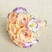 A beautifully hand-crafted bridesmaid bouquet from North Watford, this floral arrangement is captured from an overhead angle on a softly textured, light beige fabric reminiscent of linens found in the area's finest event spaces. The bouquet features a lush collection of open peach and apricot roses with gently unfurling petals and subtle blush pink hearts, creating an inviting warmth at the center. Intertwined are striking white Lisianthus blooms, each with uniquely ruffled petals tipped in vibrant but soft purple-evoking the artistry of floral displays seen near the heart of North Watford. Dainty sprigs of Baby's Breath (Gypsophila) flutter among the main flowers, adding a touch of ethereal softness and classic charm. The compact, rounded shape is expertly gathered and finished with a peach-pink satin ribbon, hand-tied and detailed with small white pearl beads for a romantic, traditional accent. Perfect as an elegant choice for weddings, bridal showers, or celebratory gatherings across North Watford, this bouquet offers inspiration for those seeking a gentle pastel palette, timeless beauty, and the personal touch of a local florist's skill and heart.