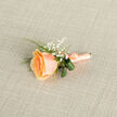 In soft, early light this peach rose boutonniere seems to glow from within, its petal layers moving from a honeyed apricot at the core to a gentle, pale peach along the tips where the light kisses each ridge. The florist's hand is evident in the careful selection: a single lush rose balanced by clusters of tiny gypsophila that sprinkle the composition with stars of white, lending an airy, dreamlike quality that reads as both youthful and profoundly refined. Curved loops of deep green foliage and a slim textural fern provide a cool contrast, their glossy surfaces and subtle veins offering depth and a quiet botanical freshness. The stem is bound in satin ribbon in complementary peach hues, wrapped and finished with a small, precise bow so the ribbon's sheen plays softly across photographs and embraces. I prepare pieces like this in our North Watford workshop with neighbours in mind; whether a guest is walking from North Watford station to a small ceremony or stepping out for a portrait on Clarendon Road, the boutonniere is intended to sit comfortably on a lapel while evoking warmth and tenderness. Its scent is faintly floral and orchard-like, enough to evoke memory without overwhelming, and the overall mood is one of reserved celebration-a delicate keepsake for weddings, anniversaries, or those quiet moments of getting ready before a cherished event in and around Watford.