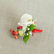 Laid carefully on a soft beige, textured fabric that resembles linen, this boutonniere is composed with attentive restraint and joyful flashes of colour. A flawless white phalaenopsis orchid claims the focal point, its broad, satiny petals unfurling in serene symmetry and revealing a gentle yellow-orange centre that lends warmth without overpowering the design. Around that core, filaments of white gypsophila create a cloud-like halo, their tiny blooms offering a light, airy lace that offsets the orchid's smooth surfaces. Clusters of vivid red hypericum berries nestle low among the greens, their polished skins catching the light and giving the piece a rustic, festive beat. Pale green buds-elongated and promising-peek through, suggesting recent gathering from the cooler corners of a local hedgerow. Glossy, deep green foliage with smooth edges frames each element, bringing structure and a fresh woodland scent to the ensemble. The stems are neatly tied with a bright red satin ribbon finished in a modest knot, the ribbon's short tail pointing to the right as though offering a small, elegant flourish.Imagined for weddings and formal nights out across North Watford, this boutonniere balances tradition and contemporary simplicity. I picture it worn by someone leaving a ceremony near Watford Junction or pausing beneath the trees of Cassiobury Park-an understated symbol of celebration, hand-assembled with the care of a neighbourhood florist who knows local rhythms and seasonal blooms.