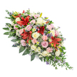 A generously proportioned double-ended coffin spray rests against a pure white background, its colours and shapes creating a serene, contemplative mood that would feel at home in any North Watford church or crematorium setting. The arrangement stretches horizontally, rounded and full at the centre with both ends finely tapered, forming an elegant, boat-like silhouette. At the heart of the design, striking red Oriental lilies open wide, their star-shaped petals rich and velvety, drawing the eye straight to the centre of the tribute. These dramatic blooms are surrounded by a profusion of roses in soft tones of cream, pale blush pink, and touches of gentle lavender, each one carefully placed so that open flowers and half-closed buds mingle, hinting at both memories cherished and moments left unsaid. Pale pink spray carnations scatter through the composition, their ruffled faces adding generous softness, as if cushioning the stronger lines of the lilies. White chrysanthemums or daisy-style blossoms sit between the larger flowers, their smaller, multi-layered petals providing delicate highlights. To add depth and a cooler contrast, the florist has tucked in blue-purple thistle heads and fine sprigs of lavender-blue filler flowers, which rise lightly above the surrounding petals and break up the colour in an artful way. All of this is supported by a deep cradle of mixed foliage-broad, glossy leaves and lighter, feathery greens that arch and extend, giving the spray a natural, garden-like feel rather than something rigid or formal. Crafted with the care of an experienced local florist, this funeral arrangement offers a graceful and heartfelt expression of sympathy, suitable for a final farewell anywhere across North Watford and the surrounding Hertfordshire communities.