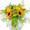 A vibrant celebration of North Watford's natural beauty, this hand-tied bouquet beams with energy and rustic elegance. The focal sunflowers, with their glowing yellow petals and rich, chocolate centers, are framed by billowy tufts of yellow filler flowers and softly blushing coral-orange accents tucked between arcades of wild, verdant foliage. Expertly placed fern fronds fan out, their delicate filigree diffusing the sunlight that floods through windows along St Albans Road, while bluish eucalyptus leaves bring a cool modern edge to the scene. The clear, round vase offers a peek at the bouquet's strong, crisscrossed stems, hinting at the craftsmanship and care behind each bloom. This arrangement exudes cheerful warmth-like a summer afternoon spent with friends at Oxhey Park-making it an uplifting gift for birthdays, a spontaneous gesture of encouragement, or simply to inject a burst of optimism into local homes and offices. The subtle green aroma and bright palette transport nature's serenity right into your living space, ensuring every day in North Watford starts or ends on a radiant note.