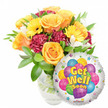 A bright, uplifting Get Well Soon gift ensemble photographed against a crisp white background: a lush glass-vase bouquet sits slightly left-of-center, spilling warmth and texture while a shiny round Mylar balloon nestles to the lower right. The arrangement is full and generous - several large, soft orange and deep yellow roses open in voluminous spirals, their velvety petals catching a soft morning-side light and suggesting a gentle, citrus-tinged fragrance. Sunny yellow gerbera daisies with clear dark centres punctuate the composition like little suns, while ruffled burgundy-to-maroon carnations add plush depth and a tactile contrast that grounds the palette. Small sprays of white alstroemeria thread through the massed blooms, offering delicate star-shaped notes and a lift of brightness. Abundant green foliage - glossy, varied-leaf textures - frames and cradles each blossom; stems and clean water are visible through the clear glass vase, lending a fresh, honest feel. The companion Mylar balloon is metallic silver, reflecting light and acting as a playful backdrop: its centre shows a cluster of cartoon-style balloons in bright blue, purple, green, pink and yellow, some patterned with stripes and polka dots, and bold yellow-and-blue lettering with a soft shadow reads Get Well Soon. Tiny starbursts dance along the balloon border and a small KALEIDOSCOPE logo sits at the very bottom edge. As a local florist's composition, this pairing reads as a thoughtful, cheering gesture for someone convalescing - the scent, colour, and craftsmanship together feel like a sunny visit from Cassiobury Park, meant to convey comfort and a speedy return to good health.