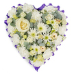 A striking heart-shaped funeral tribute dominates the frame, set against a pure white background that emphasises every petal and curve of its carefully crafted form. The heart is completely filled with a harmonious blend of white, ivory, and soft cream flowers, arranged so densely that no base is visible, creating the impression of a single, continuous cushion of blooms. At its centre, a perfectly formed creamy white rose acts like the heart within the heart, its spiralling petals radiating quiet strength and affection. Around it, large white carnations create a plush, comforting base, their gently frilled edges overlapping like layers of soft fabric. Between these, clusters of white chrysanthemums and daisy-style sprays provide a different texture, their slender or rounded petals and pale green or yellow centres bringing a subtle brightness and life. Smaller roses, rosebuds, and delicate filler flowers in tones of cream and pale lemon are tucked here and there, suggesting whispered memories and personal tributes. Cool, blue-green eucalyptus leaves weave through the flowers, their matte, silvery surfaces adding depth and a calm, natural counterpoint to the softness of the petals. Framing the entire arrangement, a deep lavender to rich purple ribbon is gathered into a continuous ruffled border, crisply outlining the heart shape and adding a solemn yet elegant touch of colour. The piece feels like it has been thoughtfully arranged by an experienced North Watford florist for delivery to a local chapel or crematorium, a classic symbol of love, loss, and dignified remembrance for a final farewell.