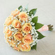 This arrangement presents a portrait of refined tenderness: a compact cluster of peach-hued roses, each bloom composed in classic form so their creamy petals overlap in layered, inviting spirals. Interlaced throughout are clouds of white gypsophila - baby's breath - which introduce a playful, airy contrast to the roses' softness and allow the eye to travel across the bouquet like sunlight through lace. Glossy, deep-green foliage anchors the composition, the leaves arranged to offer structural support while preserving the bouquet's rounded silhouette. The stems are carefully wrapped in a textured peach ribbon embroidered with pearls, a finishing touch that catches gentle daylight and gives the tie a tactile, heirloom feel. Photographed under soft, diffuse light, the roses reveal subtle tonal shifts from apricot to blush, while the gypsophila brightens the overall palette with its delicate, snowy points. There's a fresh, understated fragrance: the clean green of cut leaves blends with the rose's mild sweetness and the faint, powder-like scent of gyp, creating a scent that is intimate rather than overpowering. As a local florist familiar with marriages and anniversaries around Vicarage Road and Watford Junction, Flower Delivery North Watford often crafts this style for brides seeking a quietly romantic bouquet - one that reads as both modern and timeless. It carries the calm optimism of a new beginning, a piece meant to be held and remembered long after the ceremony's last note fades.