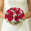 In this image, a bride holds a perfectly rounded bouquet of luxurious red roses encircled by dainty white baby's breath, the arrangement exuding timeless romance suited to a North Watford wedding. Each rose is fully open but still structured, the petals layered in tight, velvety spirals that catch the light with a gentle sheen, their rich crimson tone standing out beautifully against the soft neutrality of a white gown. Surrounding them, the baby's breath appears like light clouds of snow, each tiny blossom adding texture and contrast without overwhelming the roses, creating an effect that feels both airy and intimate. Slender stems of greenery nestle quietly at the base, grounding the bouquet with a fresh, garden-like feel reminiscent of the greenery around Watford Fields or along the paths near Garston. The bouquet's domed shape rests neatly in the bride's hands, the stems bound securely yet discreetly, allowing the flowers themselves to remain the focus. You can almost sense the weight of the roses, firm yet gentle, and imagine the subtle fragrance rising as the bride moves-sweet, floral notes mingling with the crisp scent of freshly cut foliage. The overall mood is one of calm anticipation, a still moment just before vows are spoken in a local church or registry office. Crafted with precision and an understanding of traditional bridal style, this bouquet speaks of loyalty, enduring love, and the quiet, heartfelt joy of beginning a new life together in North Watford.