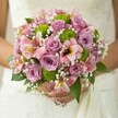 This North Watford bridal bouquet tells a story of joy, freshness, and gentle romance, artfully blending the soft lilac and blush roses at its core with the vibrant greens of round button chrysanthemums. The roses' velvety spirals open amid sprays of white baby's breath, whose tiny blooms create a luminous, cloud-like effect against the elegant backdrop of a white lace wedding dress. The arrangement feels weightless in the bride's hands, each pink alstroemeria introducing playful streaks of magenta and gold that hint at the exuberance of a Watford spring. Crisp green mums inject a lively, modern accent, while the deep green foliage provides grounding structure. With its glowing palette and tactile richness, the bouquet feels as if it carries the hopes and happiness of a bright day in North Watford-echoing the optimism found in local parks and gardens. Perfect for nuptials or any deeply meaningful celebration, the design radiates a quiet serenity, imbuing the moment with early morning freshness and the promise of new beginnings.