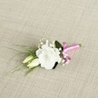 A delicate wedding boutonnière lies at a soft diagonal on a textured, oatmeal-beige fabric that looks like finely woven linen, its natural fibres catching the gentle, even light. At the heart of the design is a single white lisianthus bloom, fully open, its ruffled petals forming a layered cup that feels both graceful and contemporary, the kind of flower many North Watford couples choose for understated elegance. Just below and to the left of this main blossom, two creamy, pale-green lisianthus buds rest closely together, their smooth, tapered forms suggesting blooms that will unfurl later in the day. Threaded between them, cloud-like sprays of tiny white gypsophila add a misty softness, echoing the lightness of the spring air you might feel walking through nearby Cassiobury Park. Slim, grass-like strands of dark green foliage sweep outward towards the lower left corner, giving the piece a sense of movement and flow, while a broader, deeper green leaf tucked behind the lisianthus provides a solid, grounding backdrop. The exposed stems are gathered neatly at the lower right and wrapped in a bright fuchsia satin ribbon, tied into a neat little bow whose sheen contrasts beautifully with the matte texture of the fabric and the fresh, velvety petals. The pink ribbon introduces a joyful pop of colour against the calm palette of whites and greens, like a playful accent peeking out from a groom's lapel at a North Watford registry office ceremony. The overall mood is romantic, fresh, and intimate, perfectly suited for a groom, best man, or prom guest wanting a small, refined floral accent that feels personal yet timeless.