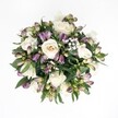 Top-down view of a hand-tied, circular bouquet resting against a pure white background, where every stem and petal stands out in crisp detail. At the heart of the design, creamy white roses unfold in soft spirals, their petals shifting gently from warm ivory to pale champagne, creating a calm, romantic focal point. Around them, deep purple and lavender Alstroemeria buds cluster in layers, many still tightly closed, with magenta veining and fresh green tips that hint at blooms yet to open. Sprays of delicate white gypsophila weave through the arrangement like a fine mist, softening the richer tones and adding a light, cloudlike texture. Dark, glossy foliage in rich emerald and forest greens peeks between the flowers and frames the bouquet, forming a natural, rounded edge that makes the central roses appear even fuller. The lighting is even and diffused, without harsh shadows, so each bloom looks freshly picked, as if it has just arrived from a morning walk through Cassiobury Park and been brought straight into a North Watford home. There is no visible vase or wrapping, just the clean geometry of the bouquet itself, making it ideal for wedding features, anniversary gift ideas, or sympathy tributes that call for understated grace. The scene suggests quiet celebration and thoughtful intention, much like a bouquet prepared by a careful local florist for same-day delivery across North Watford, between St Albans Road and Garston, to mark moments of love, remembrance, or new beginnings with a sense of calm sophistication and contemporary style.